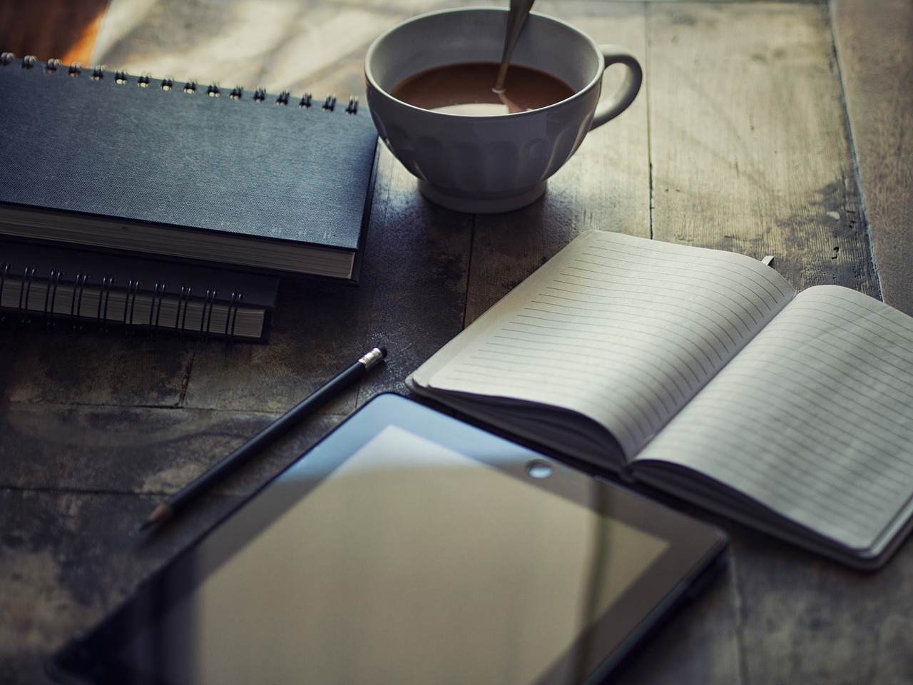Open notebook, tablet and coffee cup on a wooden desk