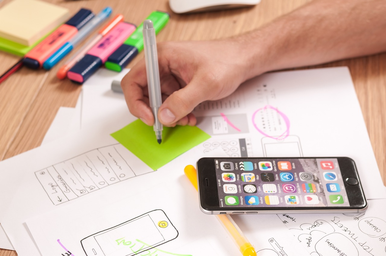 Hand sketching mobile app wireframes next to a smartphone